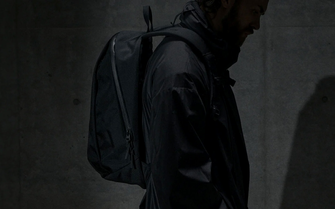 Persona de perfil con una mochila negra sobre un muro de hormigón